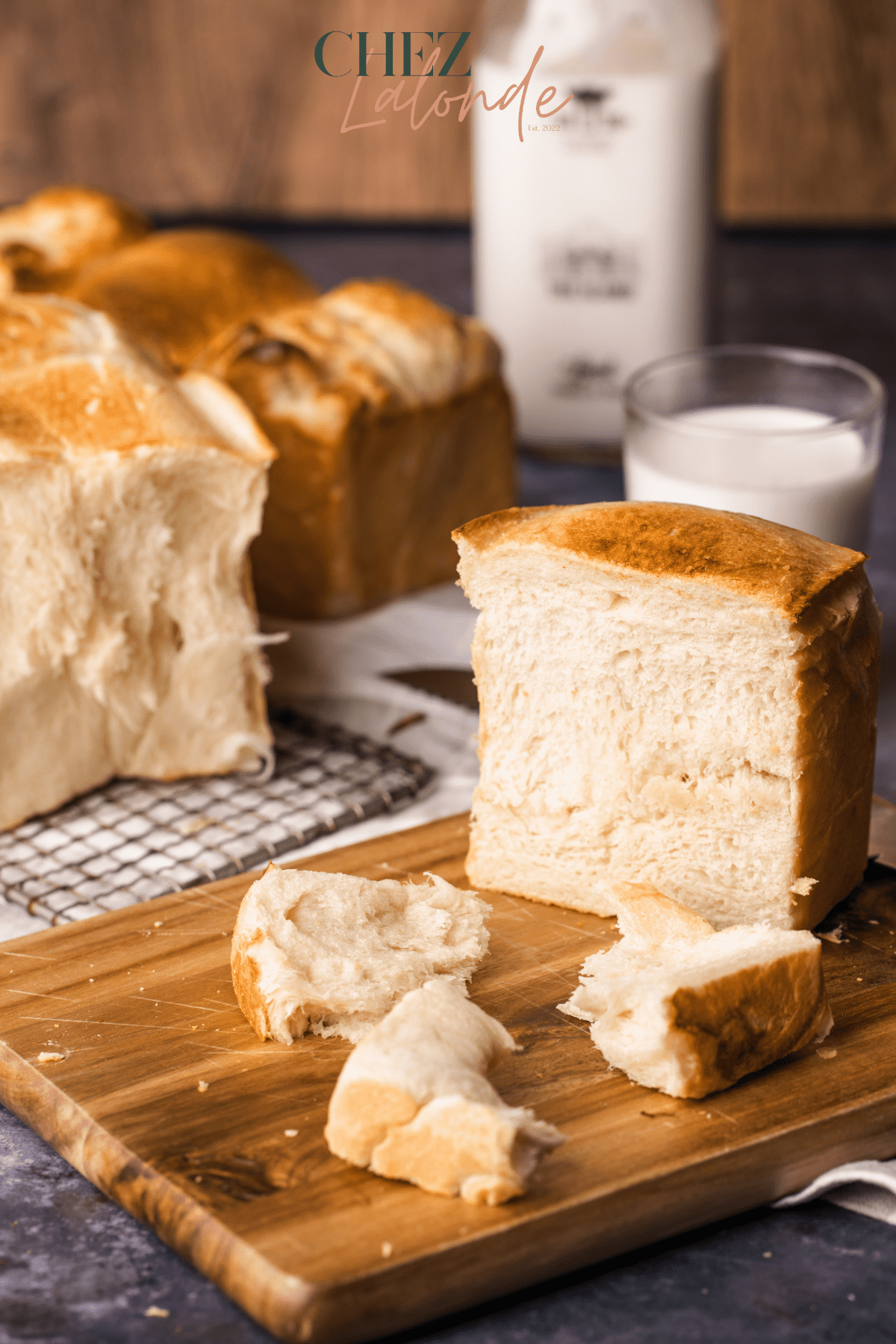 2 loafs of Japanese milk bread with a glass on milk.  Some bread is sliced to pieces. 