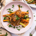 Braised beef short ribs with color carrots on round pink dish.