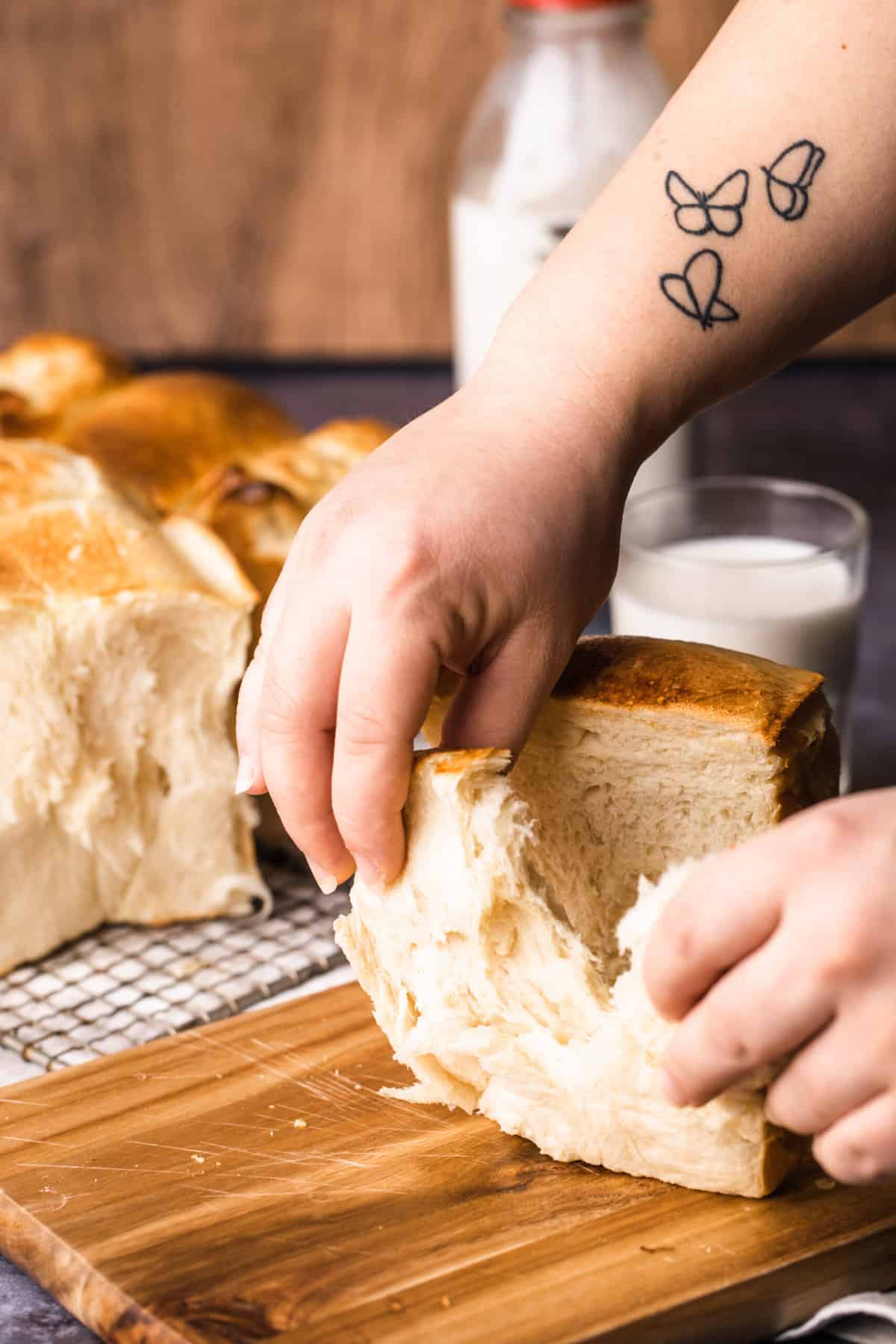 A set of hands is peeling a slice of Japanese milk bread from the loaf.