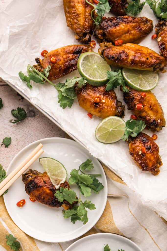 Lemongrass chicken wings with cilantro, chili peppers and lime. All are sitting on a baking tray with a pair of chopsticks