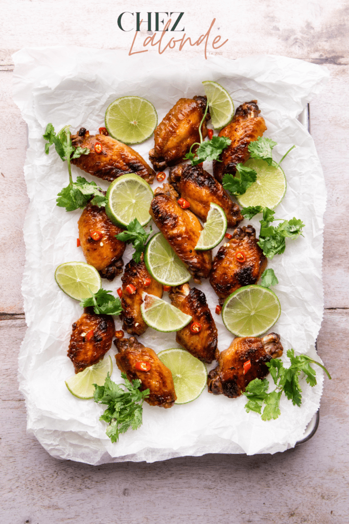 Baked Lemongrass Chicken Wings on baking tray. There are lime slices, cilantro, and Thai Chili