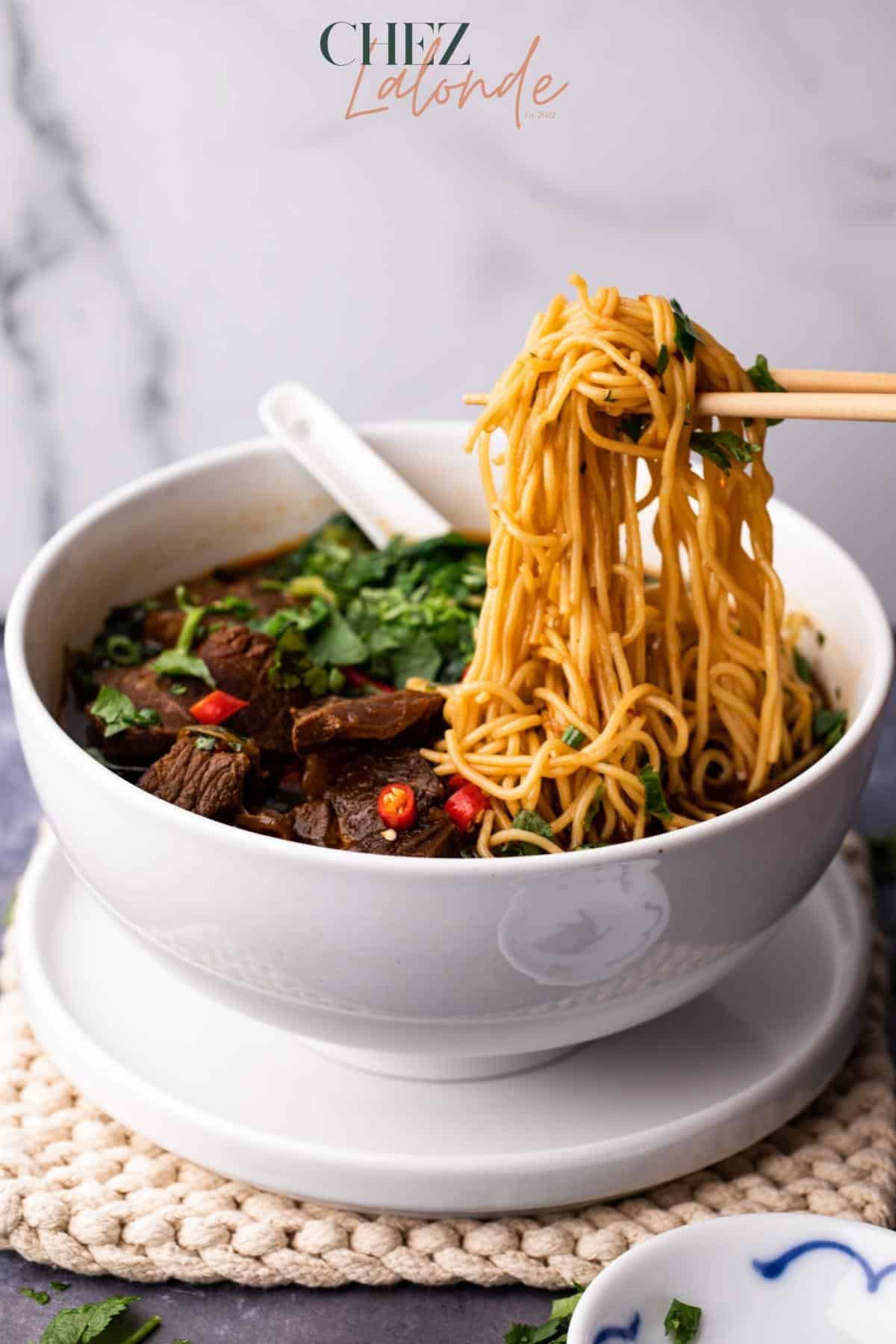 Taiwanese spice Beef noodle soup in a white bowl. Chopsticks are picking up some noodles