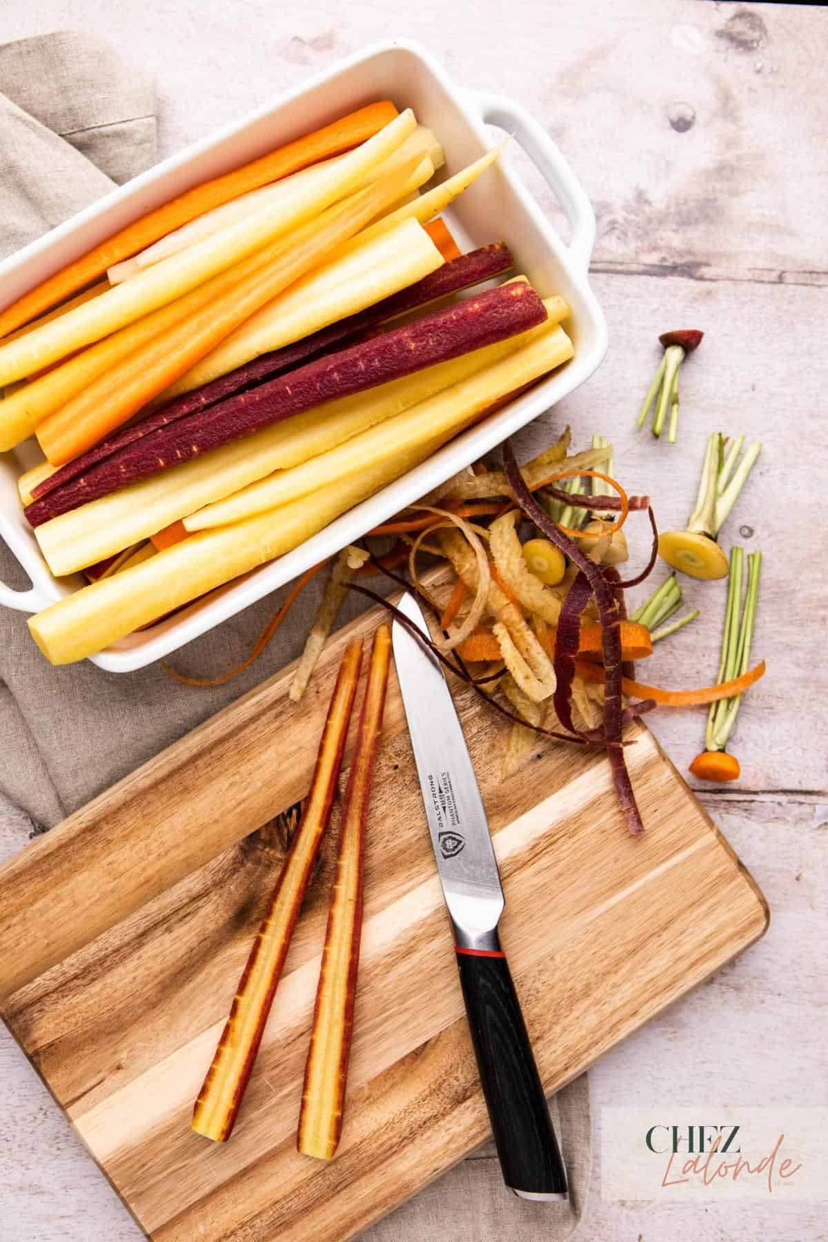 Slicing rainbow carrots in half with a knife on a small cutting board. 