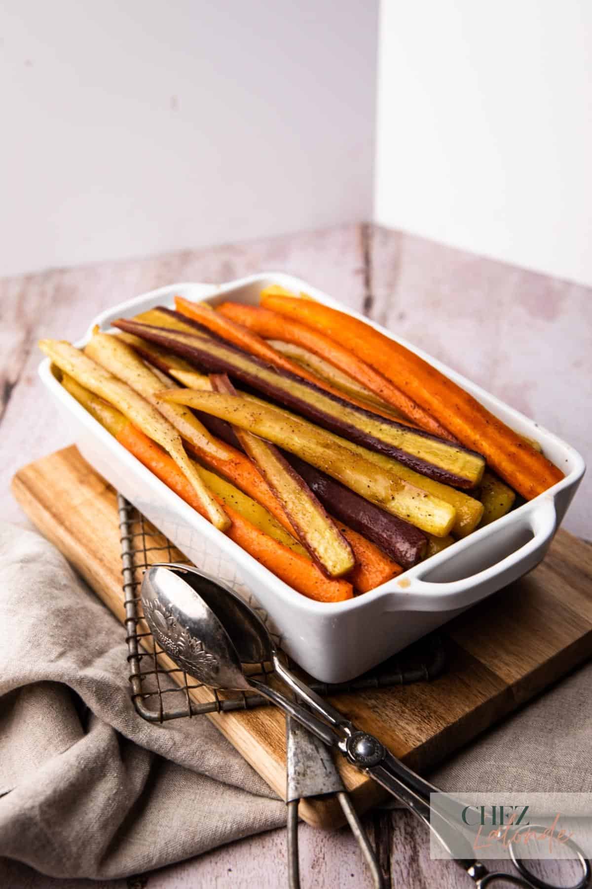 Maple Roasted Rainbow carrots in a white baking dish.  Sitting on top of a cutting board and napkin.