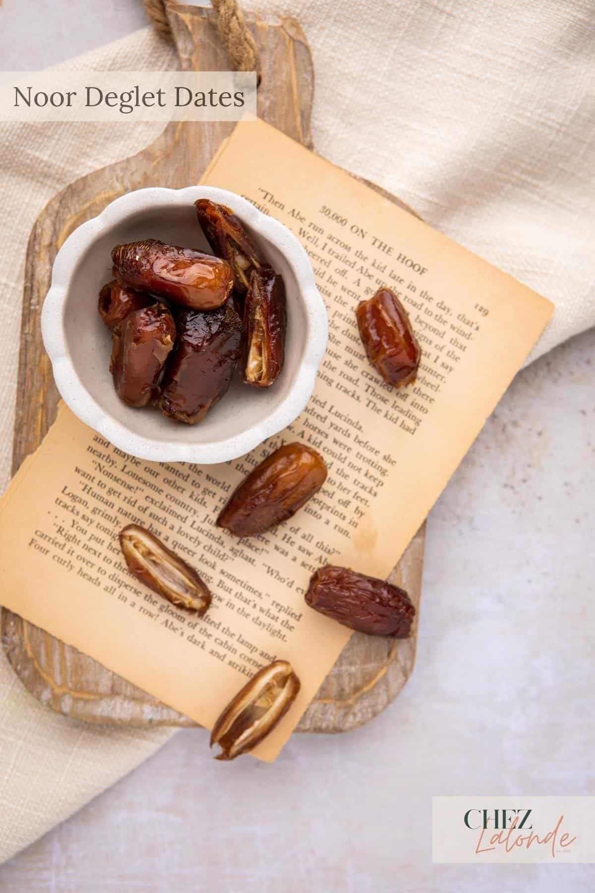 A bowl of dates sitting on top of a piece of paper and cutting board.