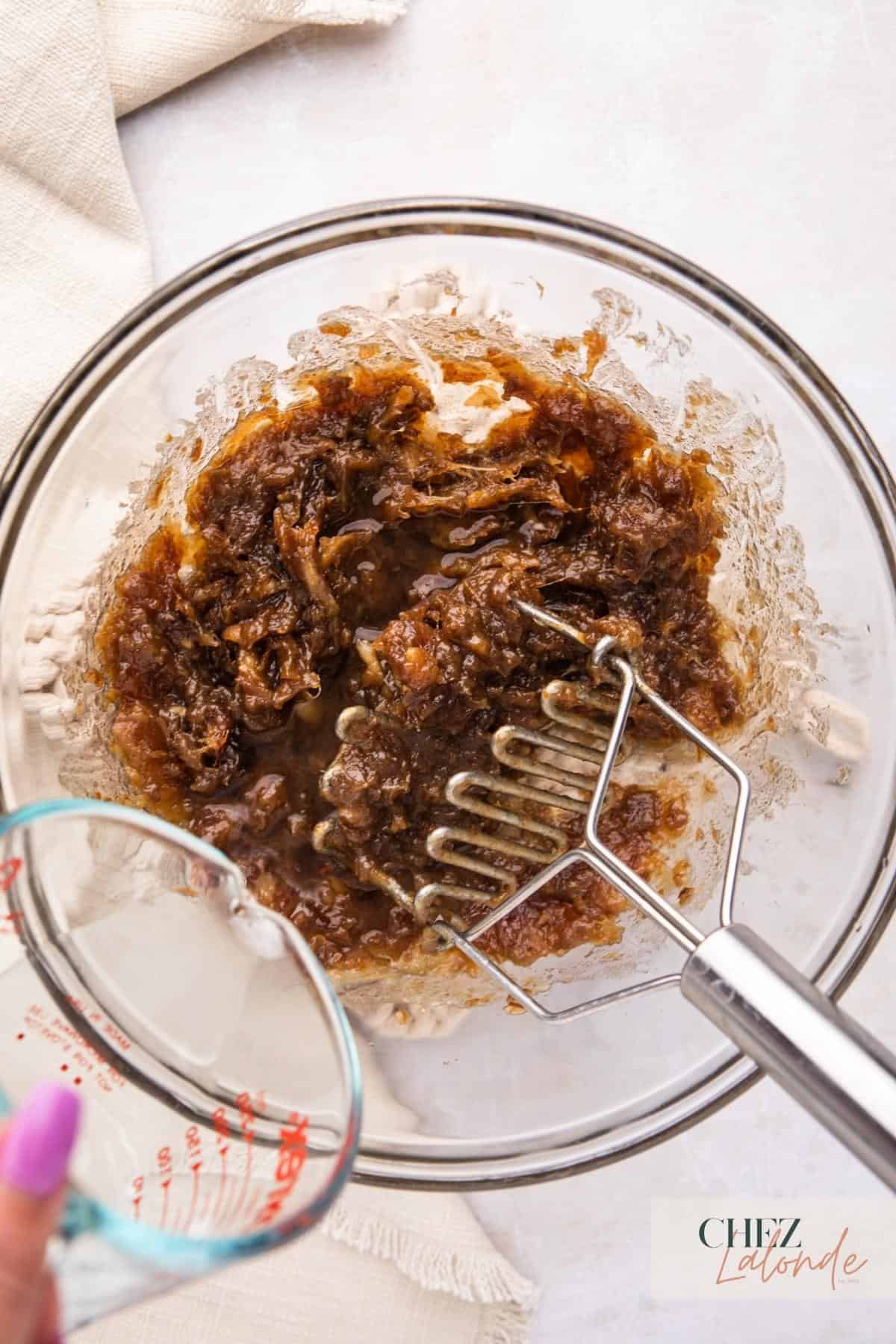 A glass bowl filled with date fillings next to a measuring cup.