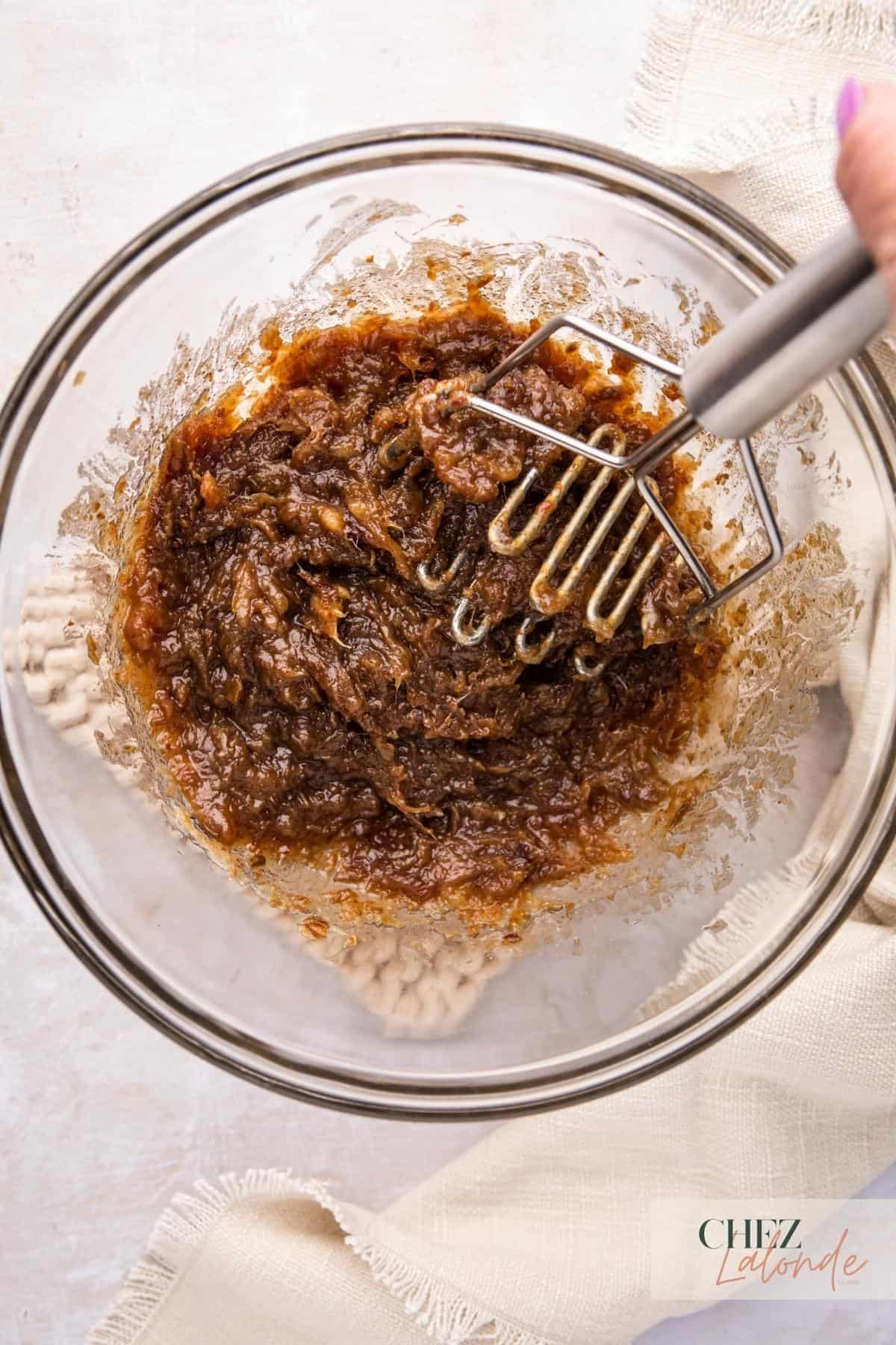A bowl of date fillings with a potato masher in it.