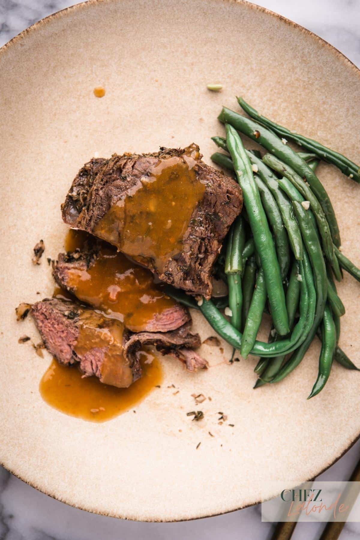 Sous Vide medium rare sous vide filet mignon with gravy and garlic green beans on a round plate