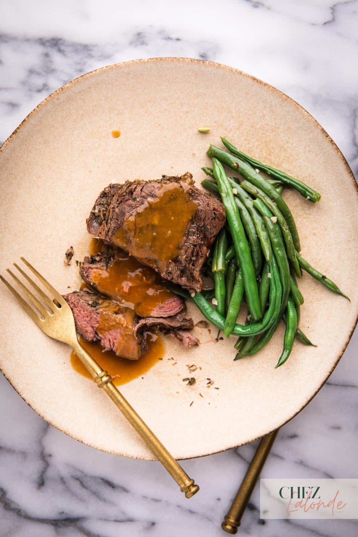 Sous Vide medium rare sous vide filet mignon with gravy and garlic green beans on a round plate and a gold folk