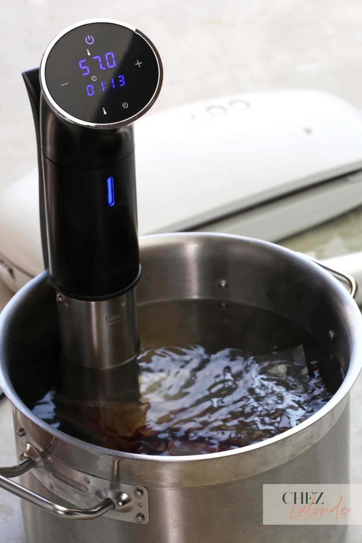 a sous vide precision cooking machine is inserted in a big silver pot with warm water bath