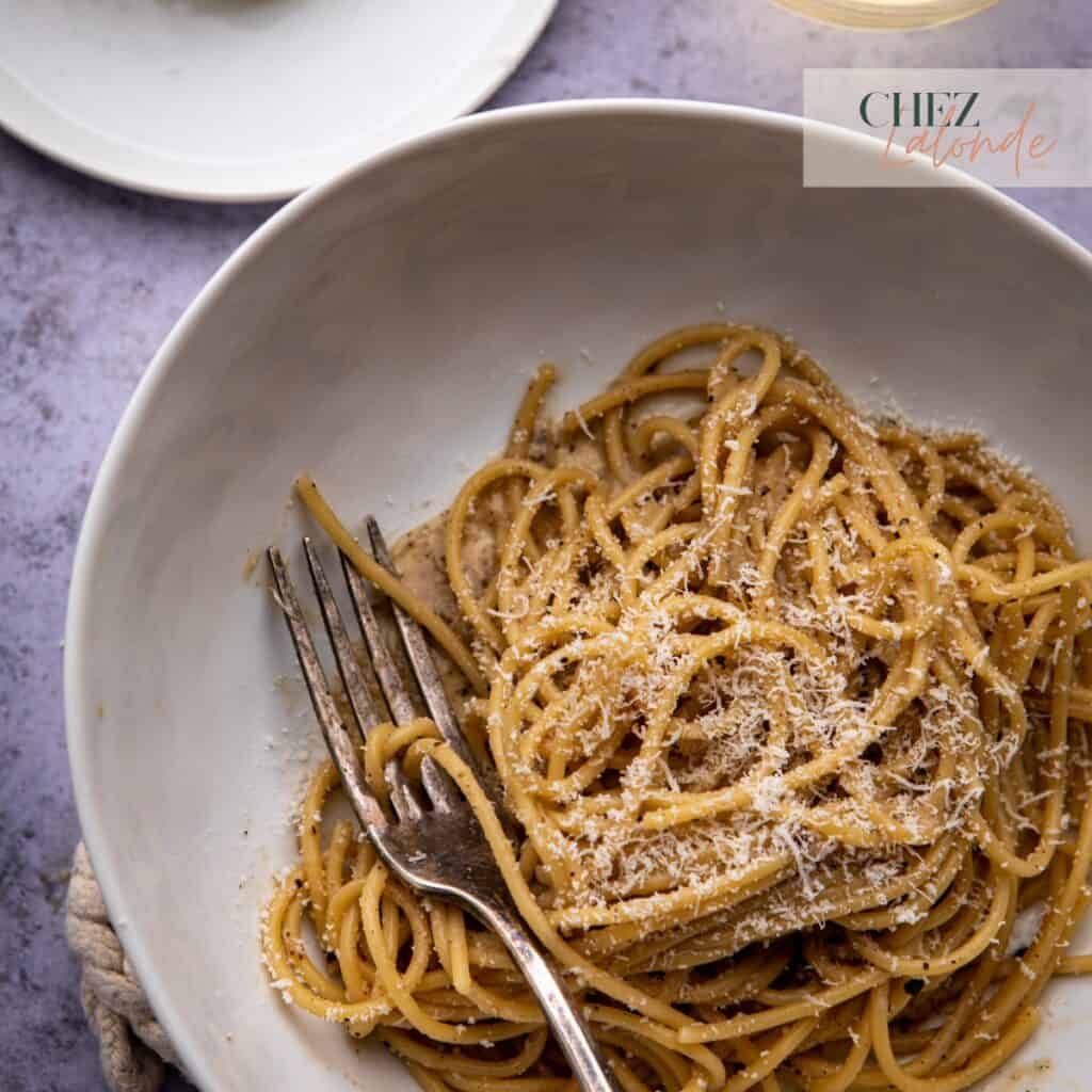 a plate of authentic Italian cacio e pepe pasta on a white bowl with a fork.