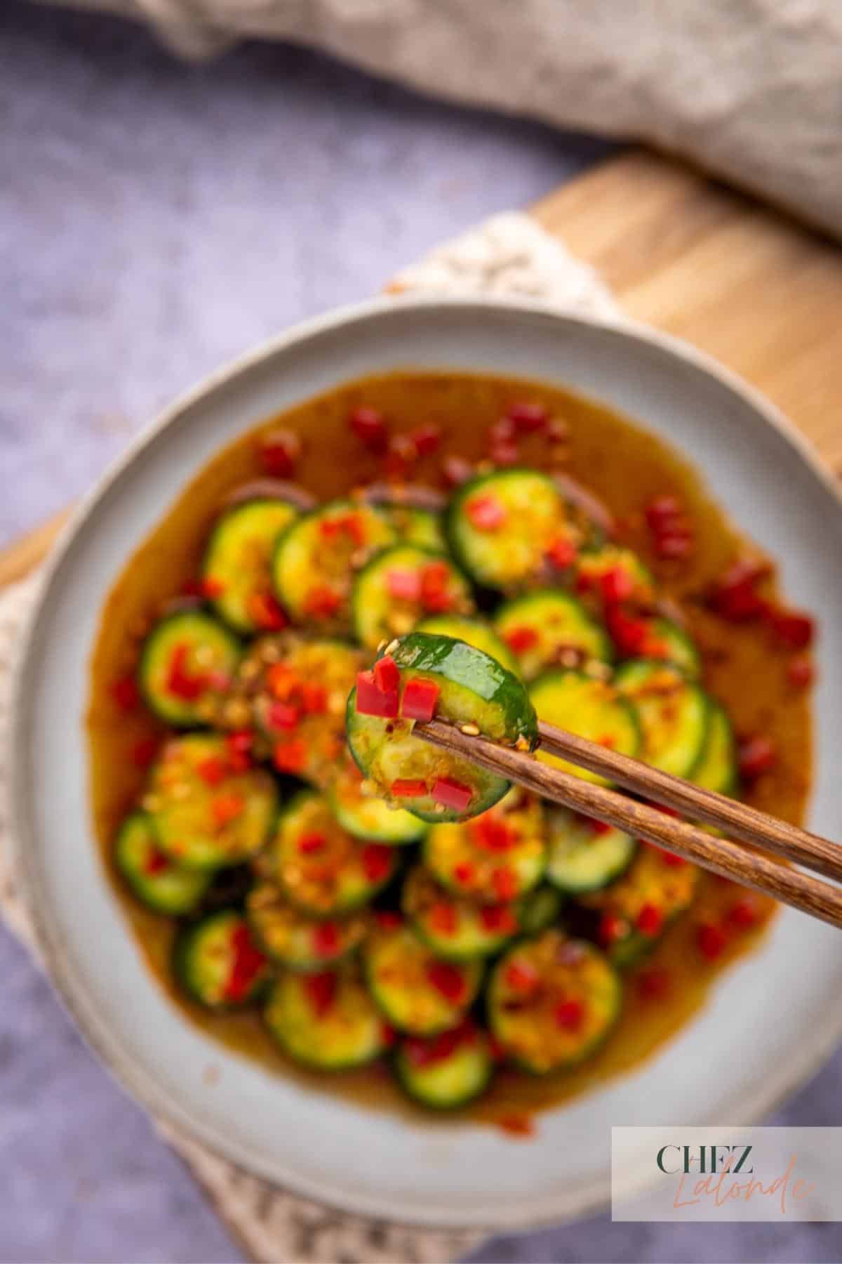 A pair of chopstick is holding a slice of Asian cucumber. 