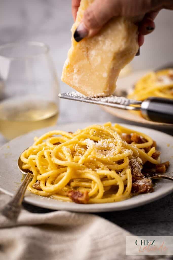 Grating Parmigiano Reggiano cheese on Carbonara pasta.
