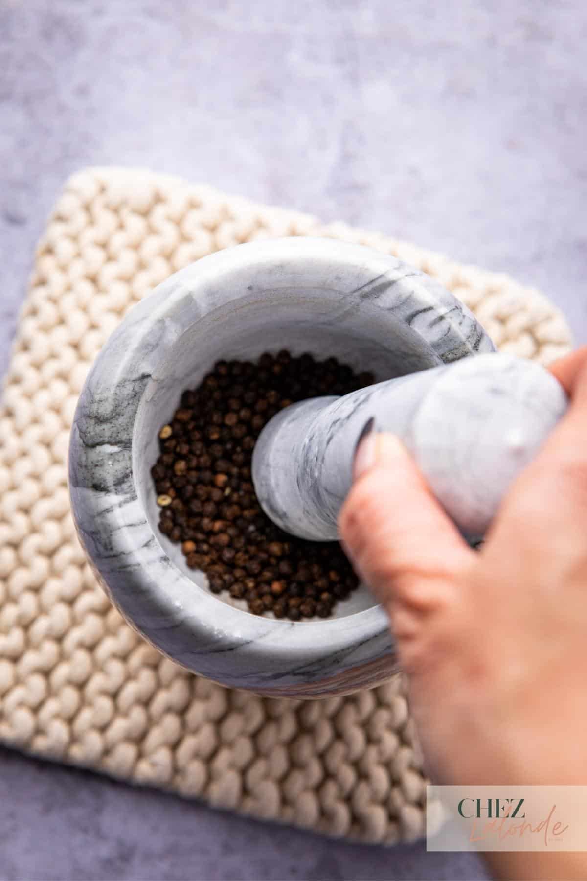 Using a mortar and pestle to crush toasted black peppercorn. 