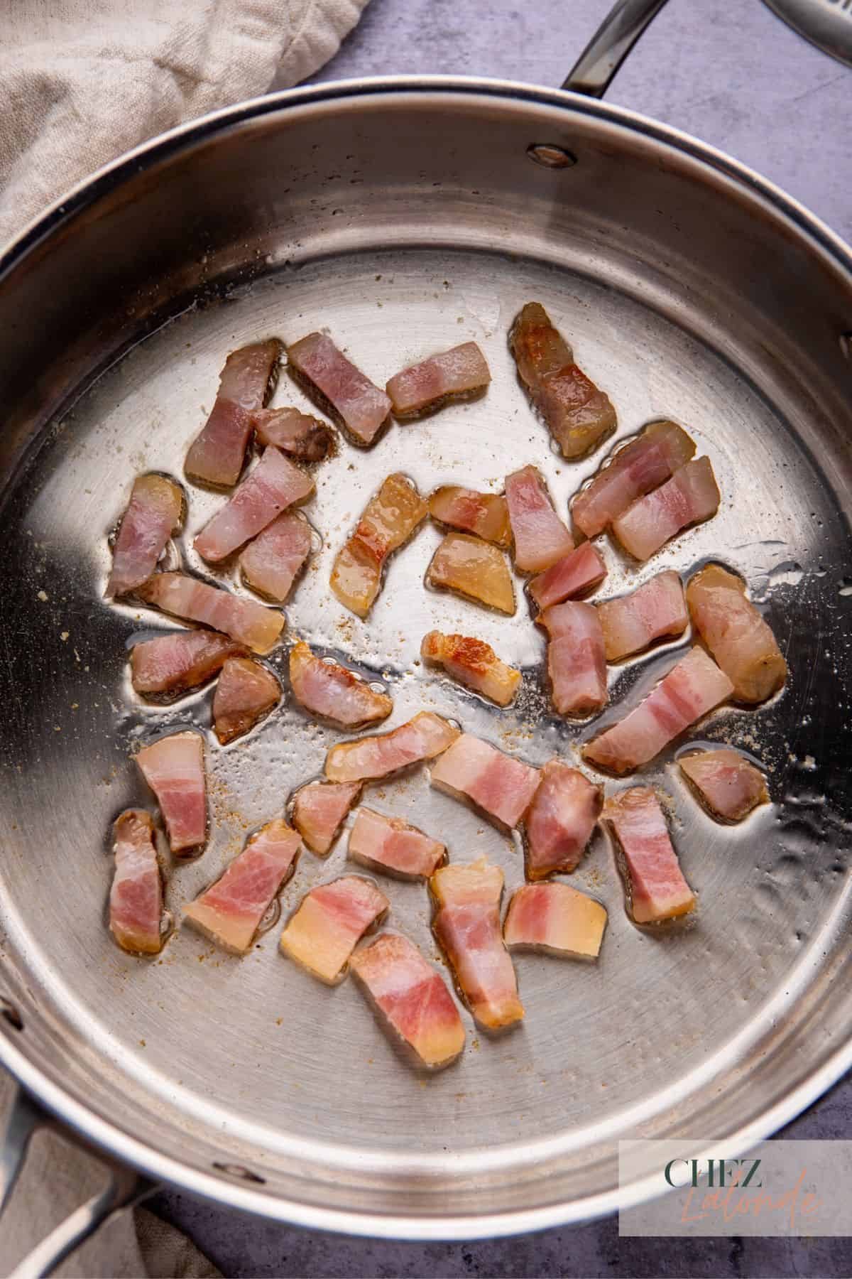 Searing strips of guanciale in a big frying pan. They are starting to cook.