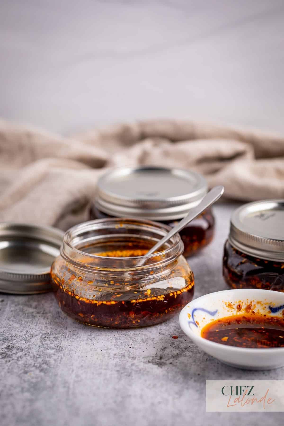 3 Mason Jars full of Chinese Chili Oil.  A little sauce plate with some Chili Oil in it and a small spoon inside of a mason jar. 