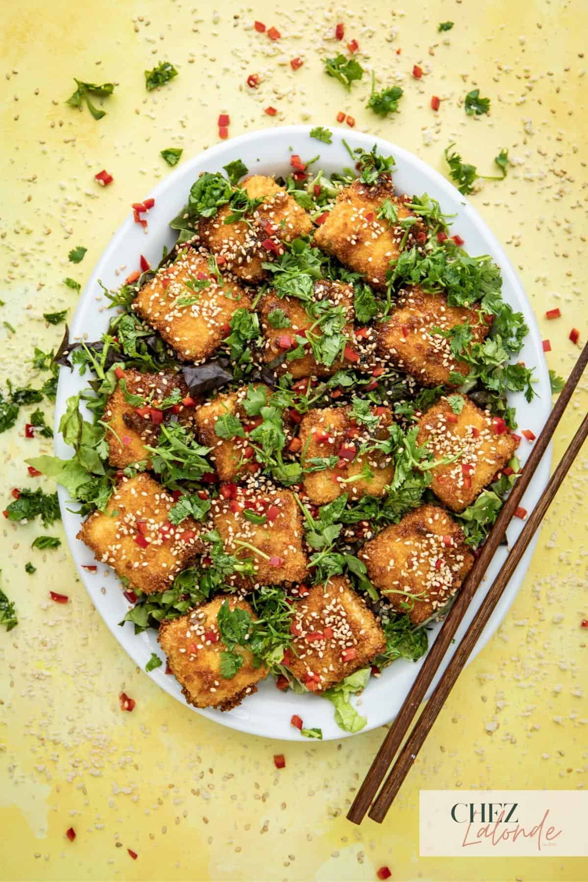 Feature image of A plate of crispy air fryer tofu with panko and drizzled in Asian garlic sauce. Tofu are on a bed of shredded lettuce.