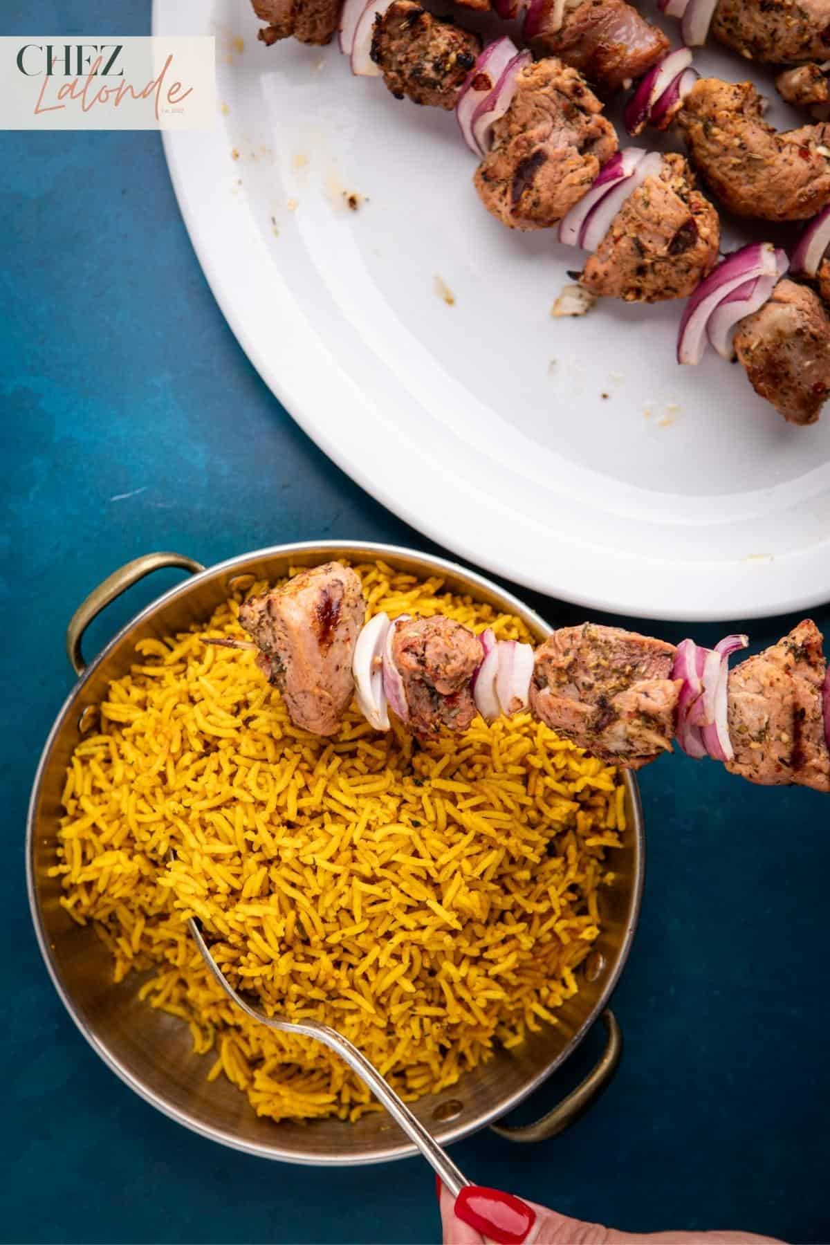 A bowl of Mediterranean yellow rice with a plate of Sous Vide Pork tenderloin Souvlaki skewer.