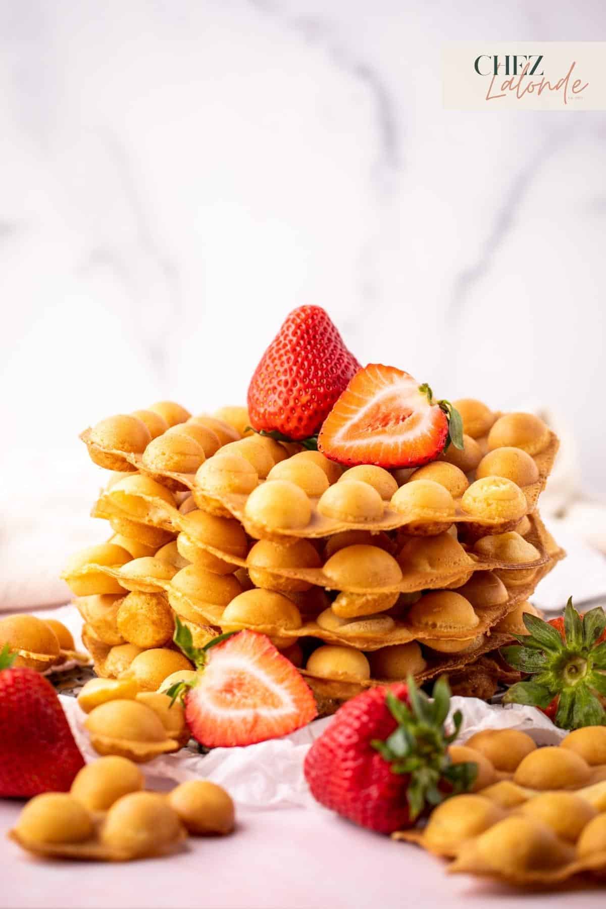 A stack of homemade Hong Kong style bubble waffles with some strawberries. 