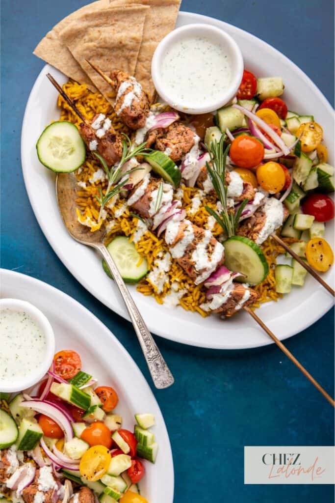 2 plates of Sous Vide pork Souvlaki with Mediterranean rice, greek salad, and drizzle with Tzatziki sauce.