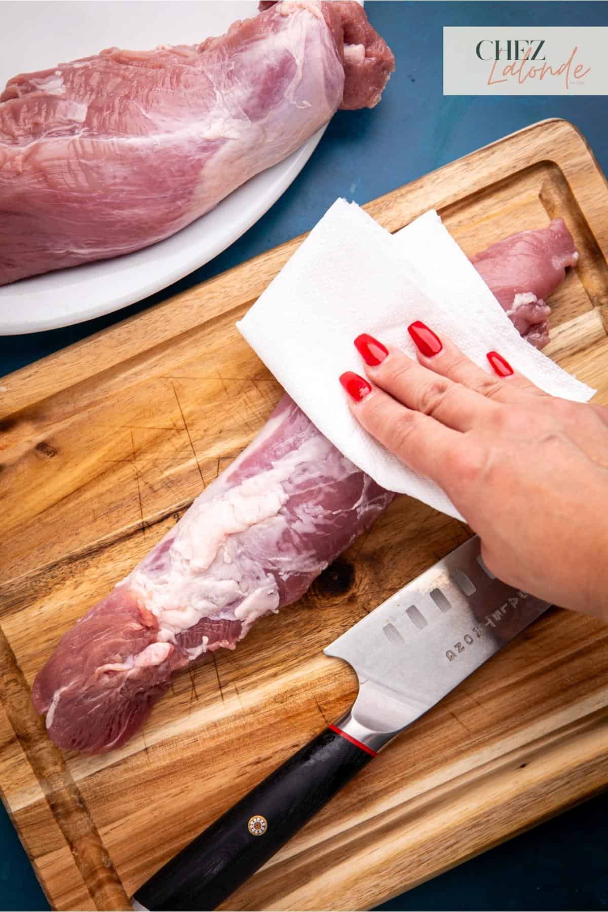 Using a paper towel to pat dry the pork tenderloin after washing it in the sink. 