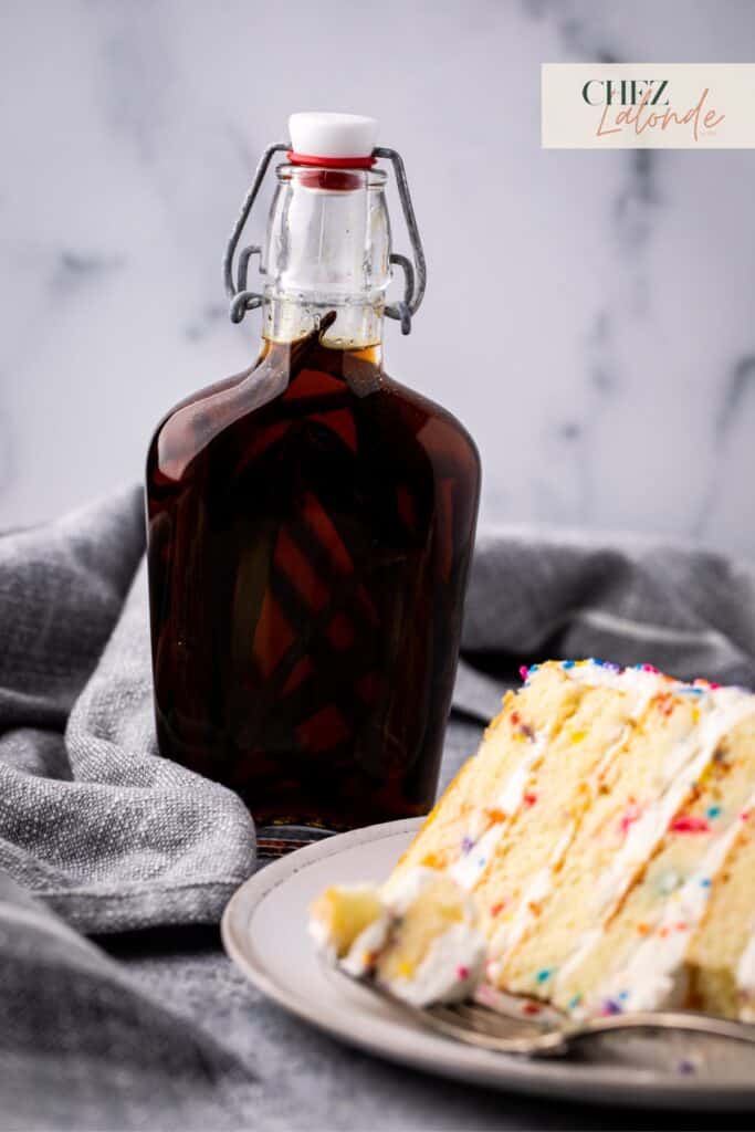 A bottle of vanilla extract with a slice of vanilla cake.