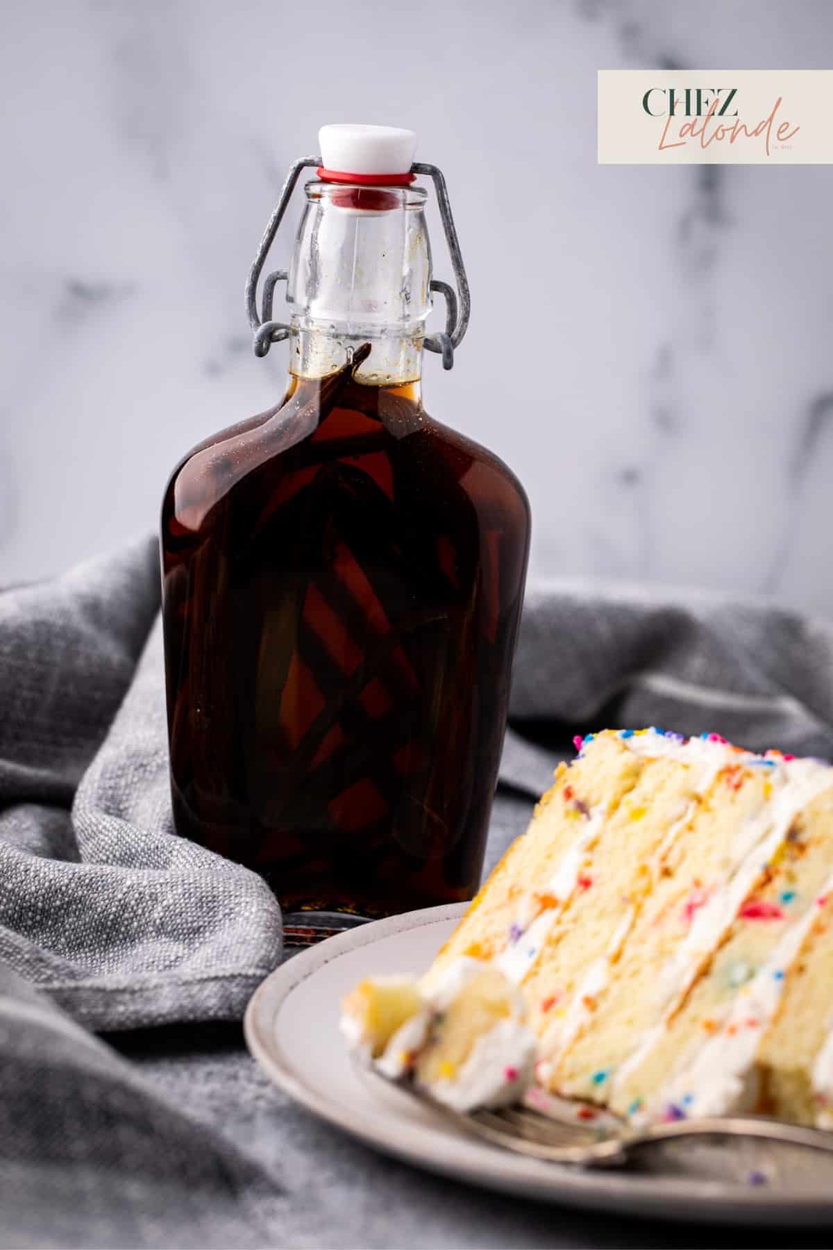 A bottle of vanilla extract with a slice of vanilla cake. 