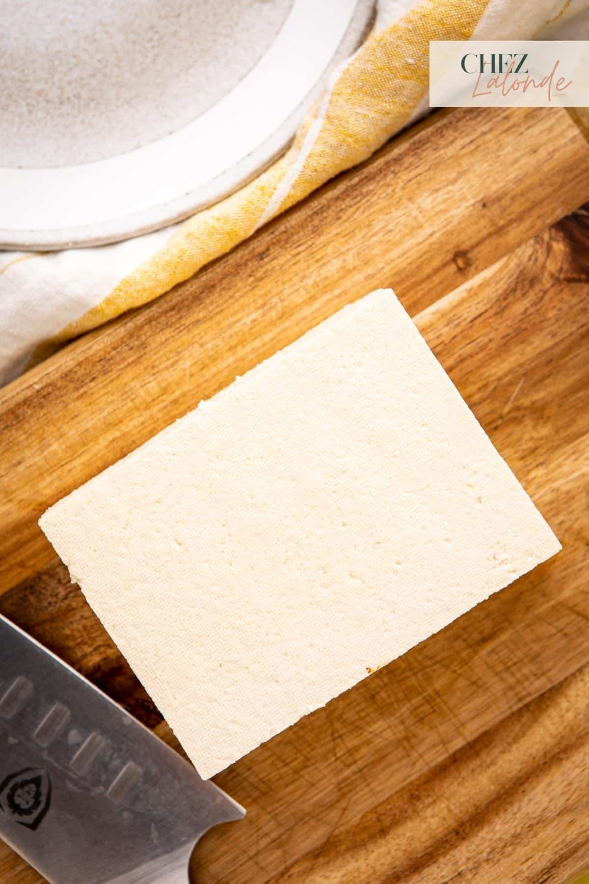 A block of firm tofu sitting on top of a cutting board. 
