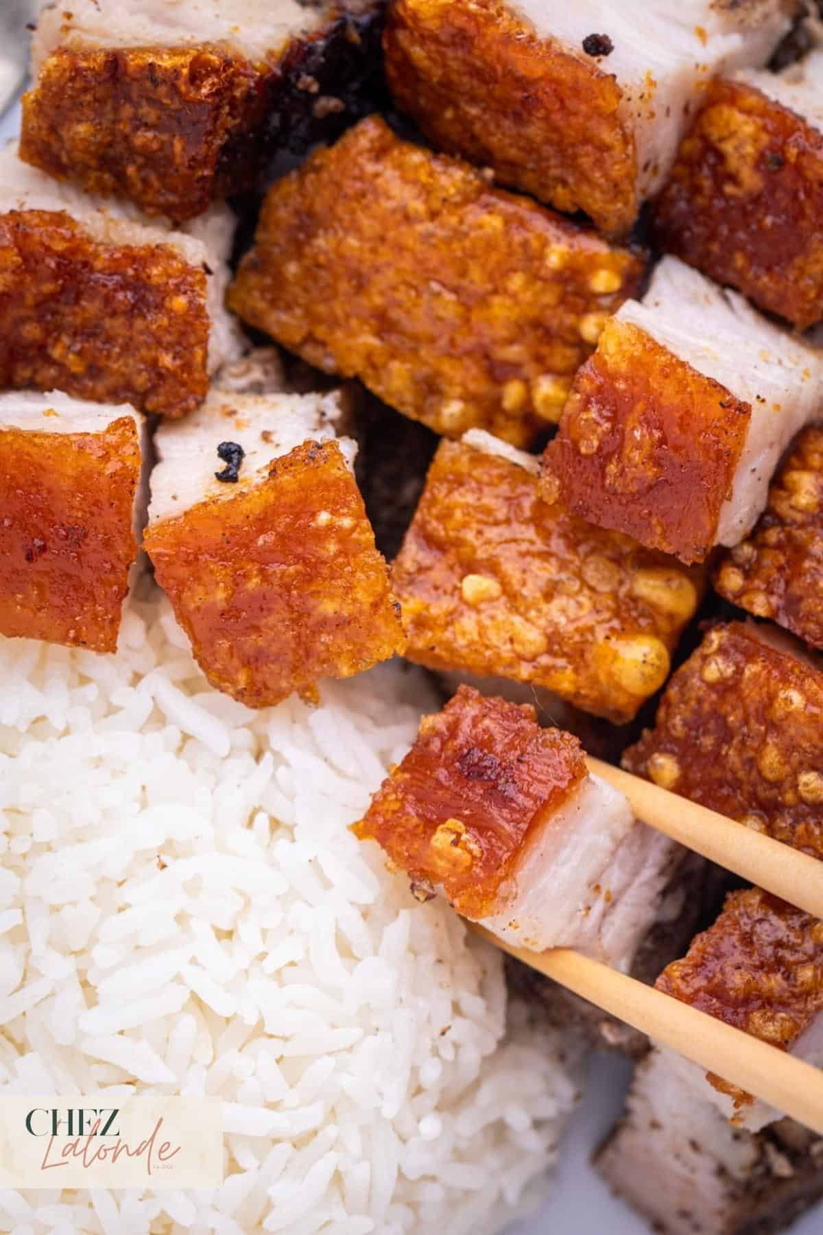 A pair of chopsticks are picking up some air fryer pork belly. 