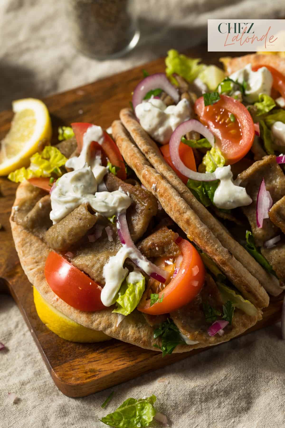 A plate of greek gyro with some tzatziki sauce and vegetables. 