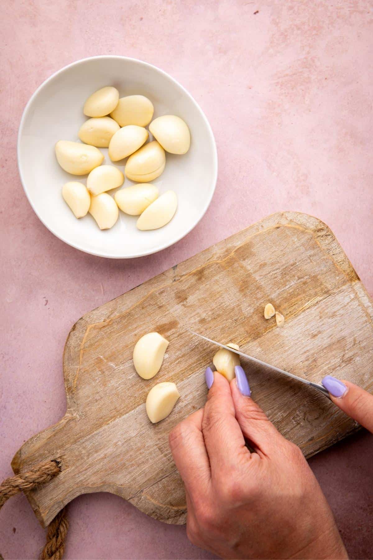 Start by peeling the skin off the garlic cloves. Place the clove on a cutting board, use a sharp paring knife to remove the root end.