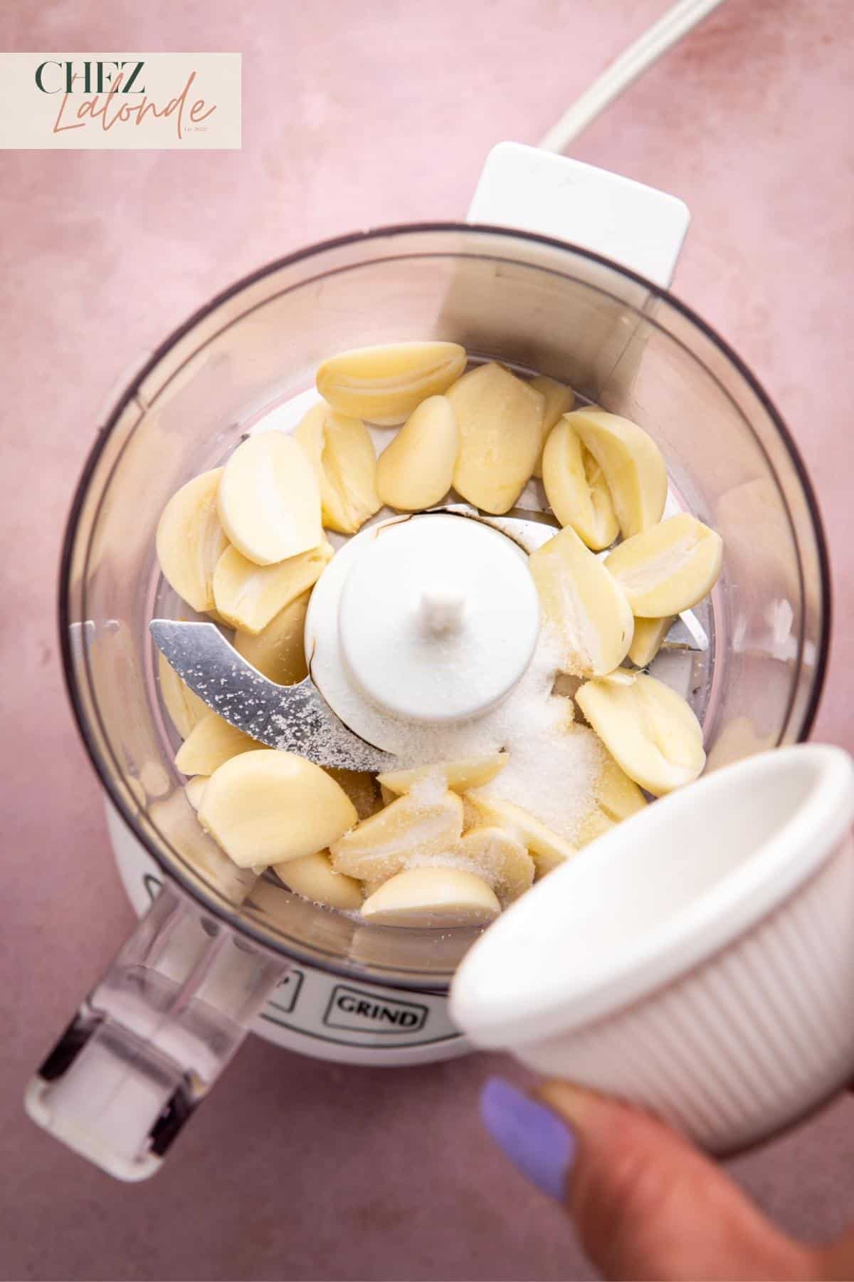 Add all the garlic cloves and half a teaspoon of sea salt to the bowl of a food processor. 