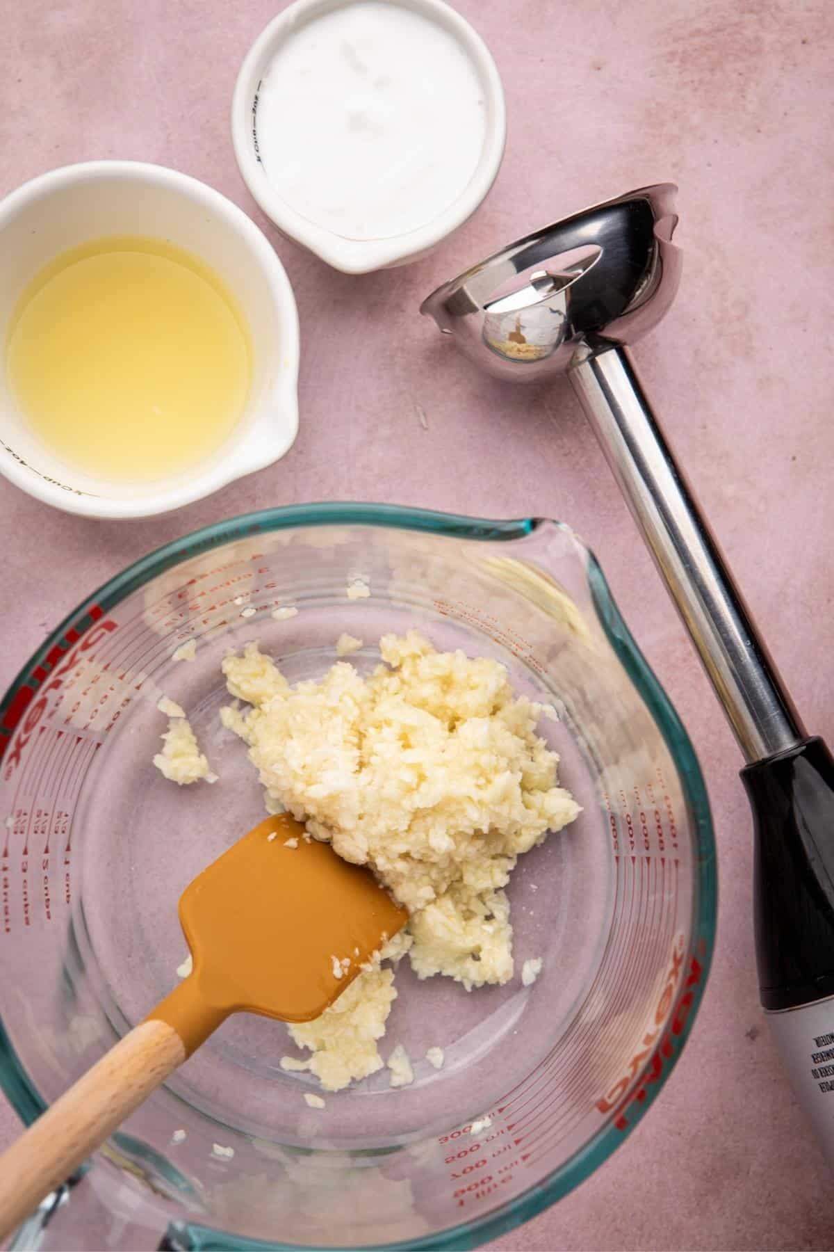 Transfer the minced garlic mixture into a deep, tall container, such as a measuring cup, to accommodate the immersion blender.
