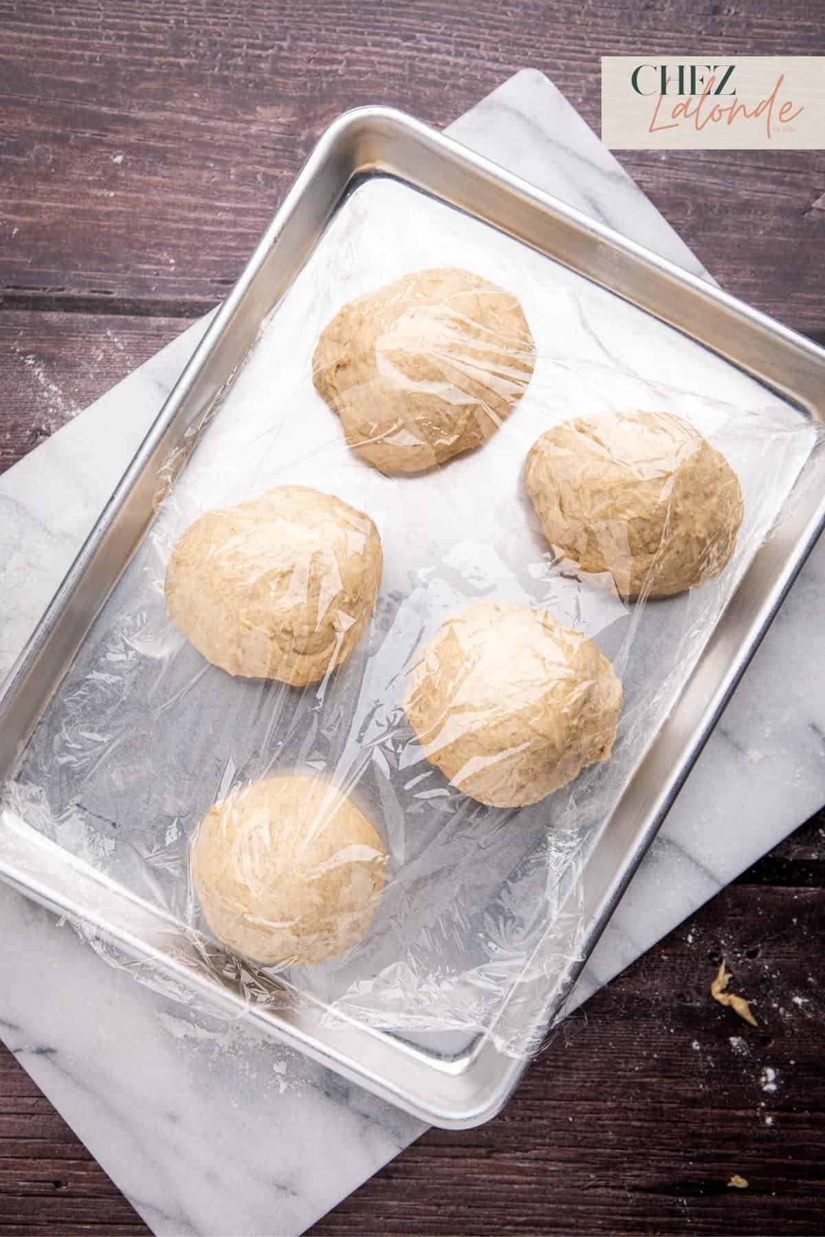 Place the dough balls on a baking sheet, cover them with plastic wrap, and return the tray to a warm spot for another 15 to 20 minutes of proofing.