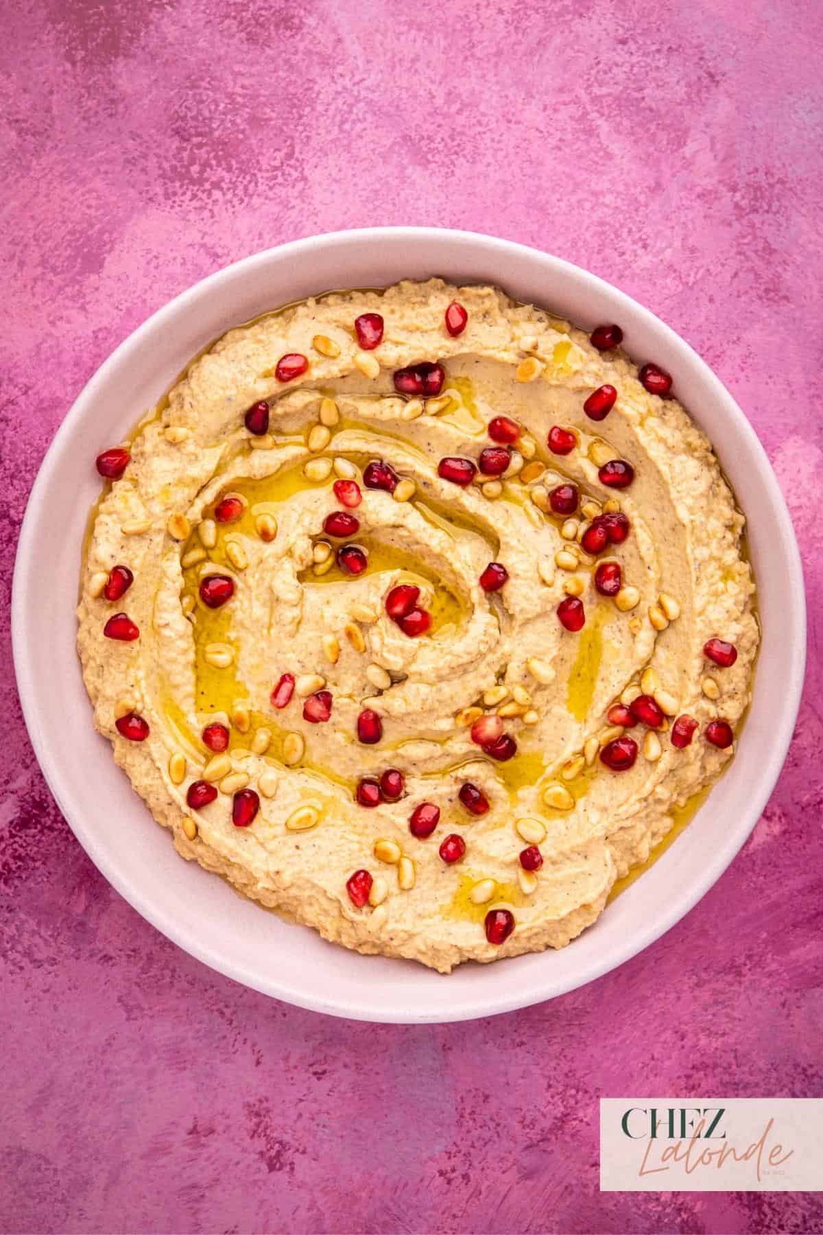 A bowl of Baba Ganoush that garnished with Pomegranate seeds, toasted pine nuts, and olive oil.