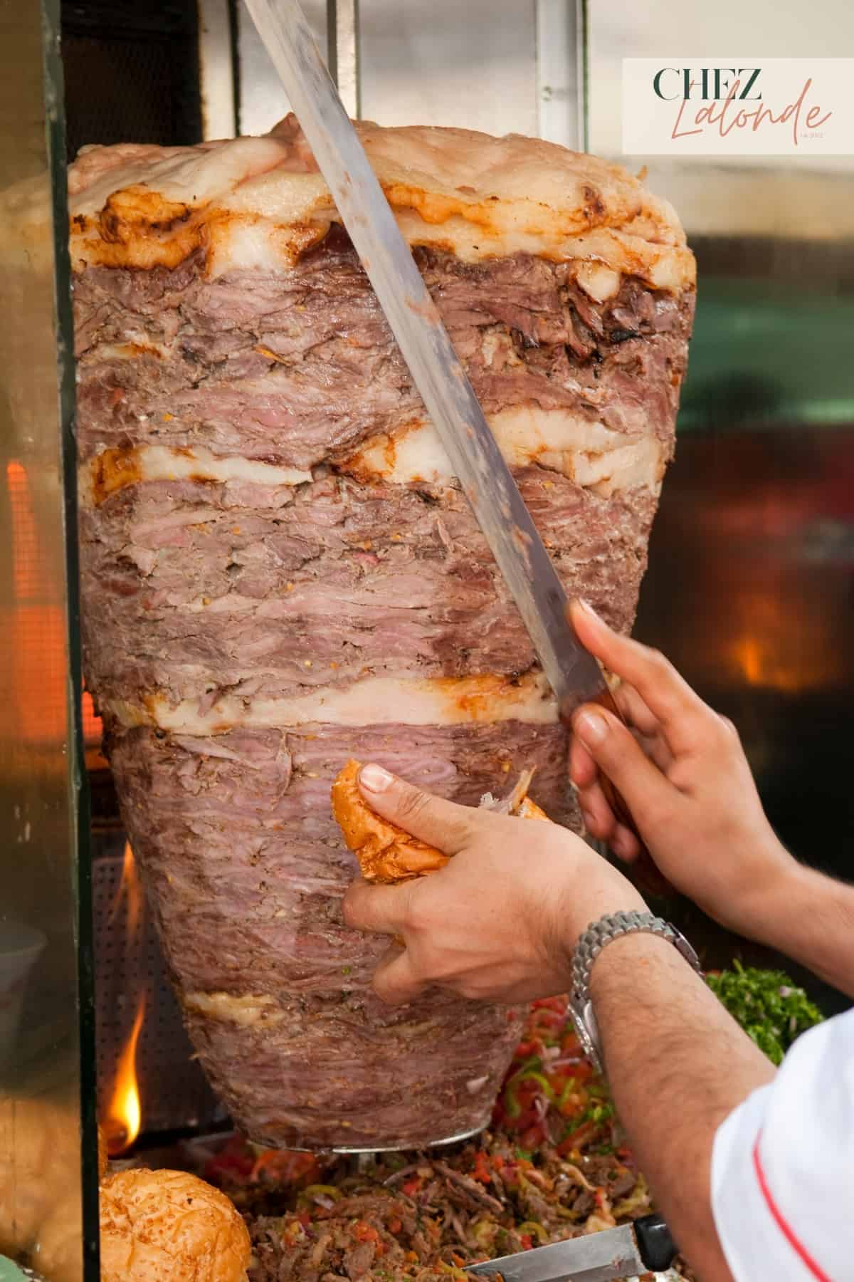 At restaurant, a chef is slicing some cooked shawarma off of the rotisserie. 
