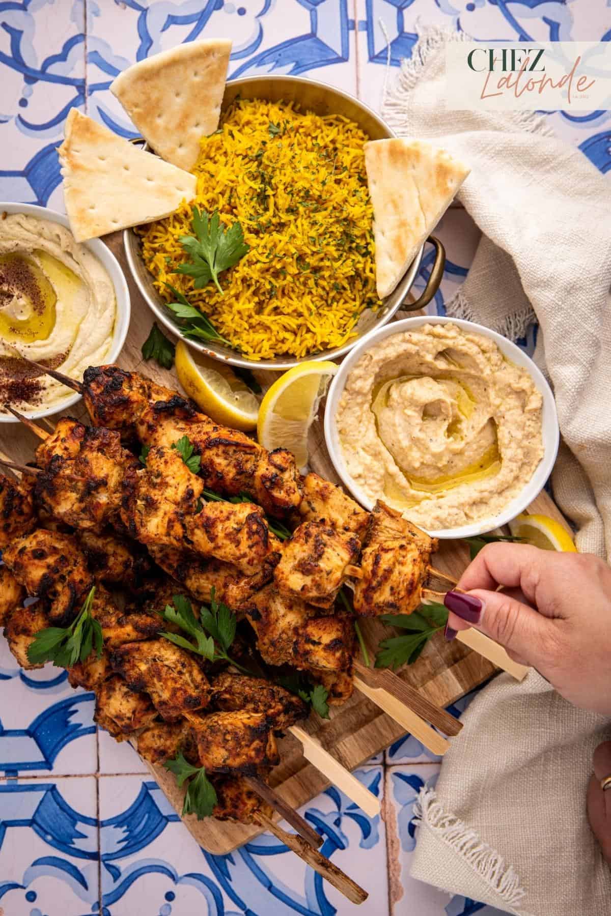a hand is picking up a Shish tawook skewer. 