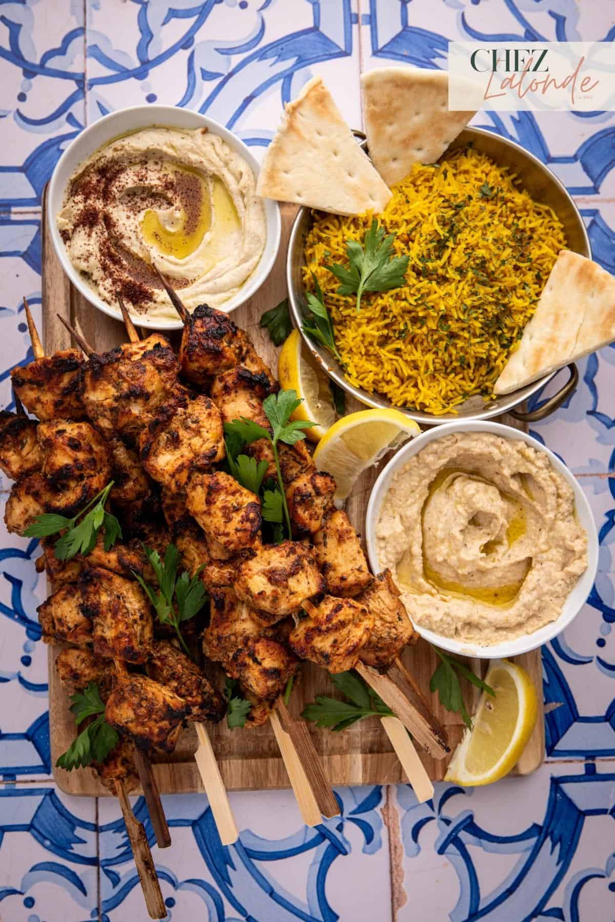 A Mediterranean style mezze platter with many air fryer Shish Tawook skewers served with yellow rice, hummus, and baba ganoush.  