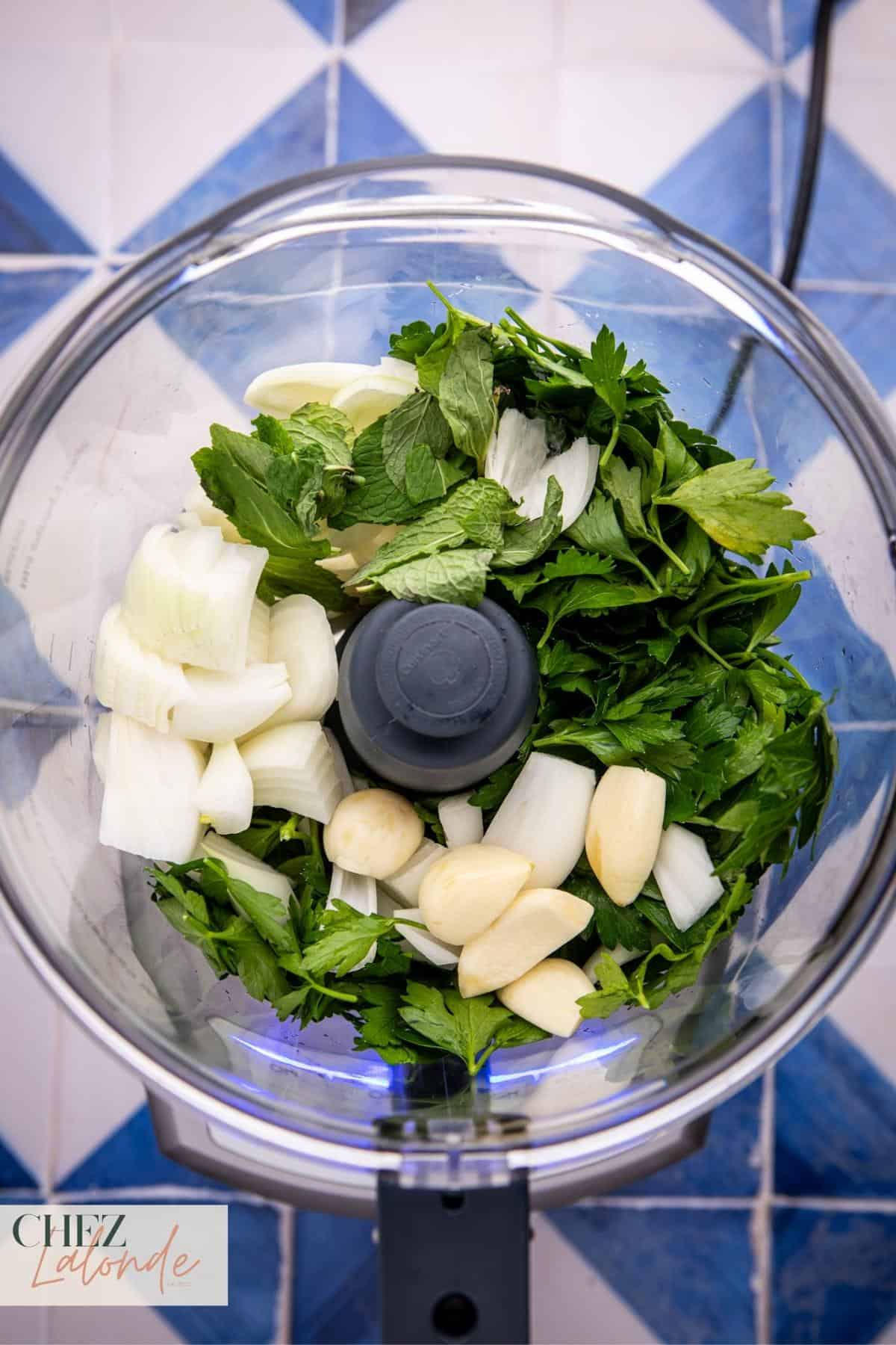 In a 16-cup food processor, combine your chopped onion, garlic cloves, mint leaves, and 2 cups of Italian flat-leaf parsley.
