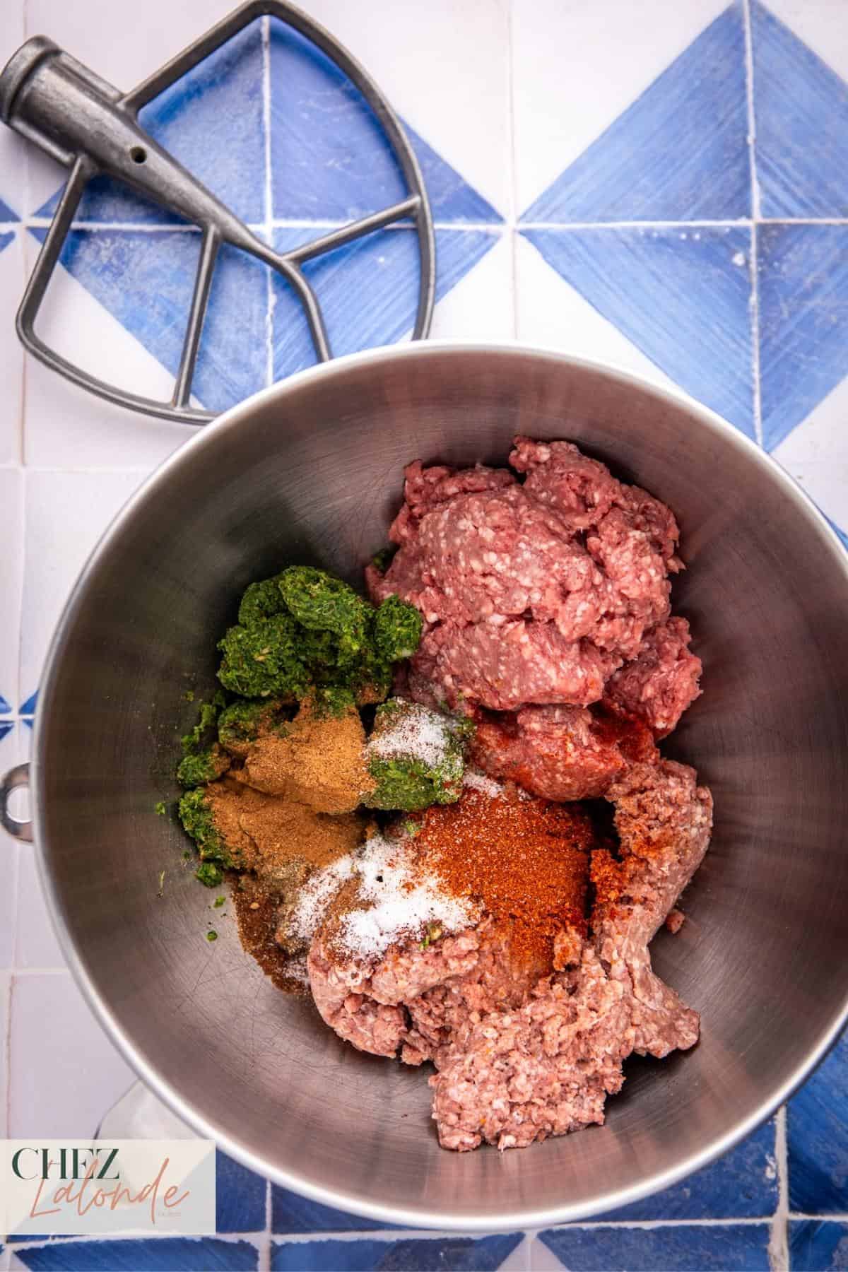 Add a pound of minced beef, lamb, herb paste mixture, and spices into the large mixing bowl using a stand mixer.